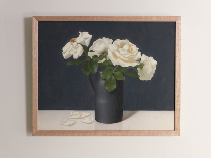 Fine art print framed hanging on a wall. The print shown is of a still life painting of white roses in a black vase with a dark blue background.