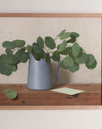 Fine art print framed hanging on a wall. The print shown is of a painting of eucalyptus leaves in a blue vase with a light background.