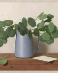 Fine art print of a painting of eucalyptus leaves in a blue vase with a light background.