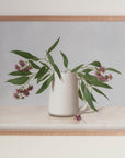 Fine art print framed hanging on a wall. The print shown is of Eucalyptus Blossom in a white vase with a light background.