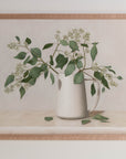 Fine art print framed hanging on a wall. The print shown is of a still life painting of Eucalyptus in a white vase with a light background.