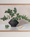 Fine art print framed hanging on a wall. The print shown is of a still life painting of Eucalyptus in a black vase with a light background.