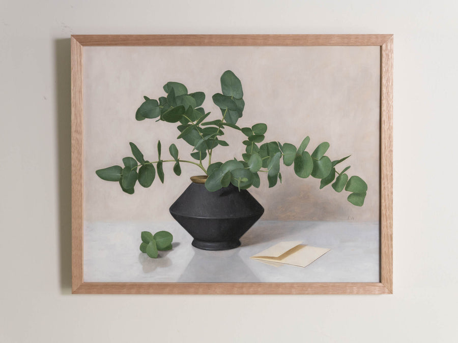 Fine art print framed hanging on a wall. The print shown is of a still life painting of Eucalyptus in a black vase with a light background. 