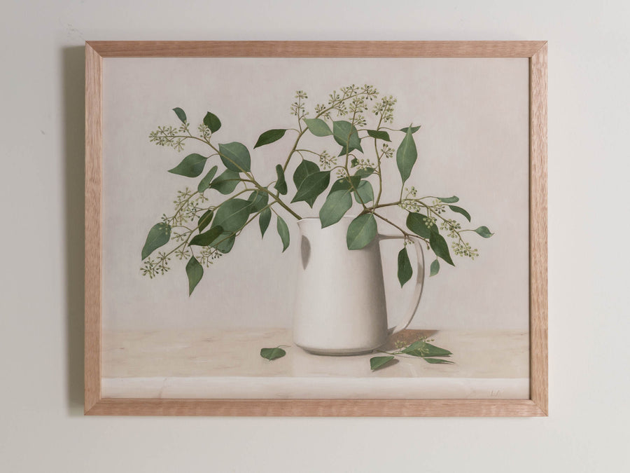 Fine art print framed hanging on a wall. The print shown is of a still life painting of Eucalyptus in a white vase with a light background. 