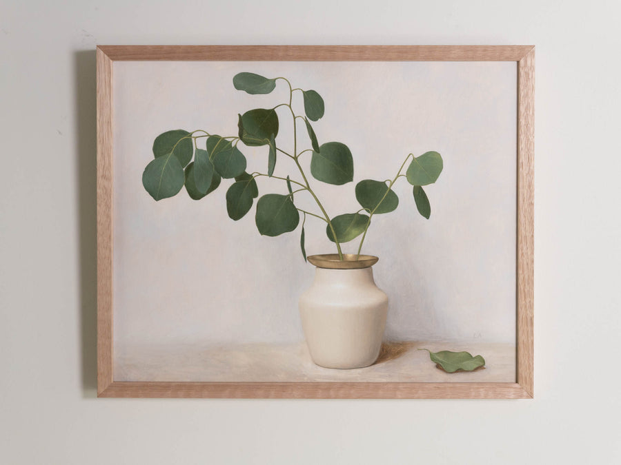 Fine art print framed hanging on a wall. The print shown is of a painting of Eucalyptus in a white vase with gold detail and a light background.