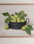 Fine art print framed hanging on a wall. The print shown is of a black bowl of green apples with a light background.