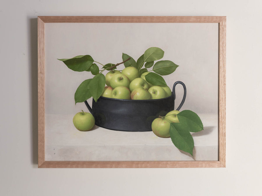 Fine art print framed hanging on a wall. The print shown is of a black bowl of green apples with a light background.